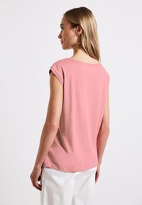 Rosa kortärmad t-shirt i bomull med rund halsringning. Bakpartiet är något längre, med en slät yta och minimalistisk design.