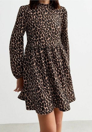 Frau trägt ein langärmeliges, knielanges Kleid mit braun-schwarzem Leopardenmuster.