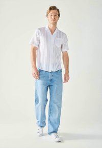 Fehér, rövid ujjú ing függőleges csíkozással, elülső zsebbel; világoskék farmer; fehér sportcipő; laza szabás, kényelmes siluett.
