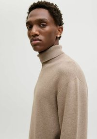 Beež turtleneck-sviiter ribakujulises tekstuuris, pikkade varrukatega ja vabalt istuva lõikega. Minimalistlik disain, ilma nähtavate mustrite või aktsentideta.