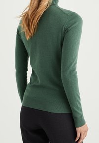 Grön, åtsittande polotröja gjord av mjukt material, med ribbat avslut och manschetter, en slät yta och minimala sömmar.