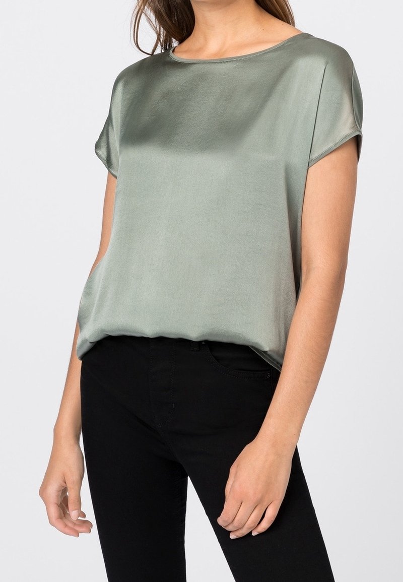 Kortärmad blus med rund hals i en mjuk salviagrön satin. Lös passform med lätt fall, kombinerad med svarta jeans.