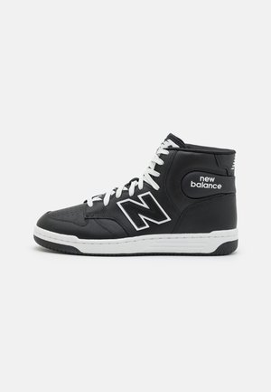 Zapatilla alta negra de cuero con cordones blancos, suela de goma y un logotipo blanco prominente en el lateral. Detalles de superficie texturizada.