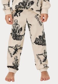 Pantalons de pyjama crème avec une texture gaufrée, ornés d'illustrations et de textes de Spider-Man en noir. Les poignets et la taille sont en noir uni.
