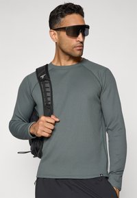 Pull-over à manches longues, texturé, de couleur vert doux, fabriqué en tissu évacuant l'humidité. Dispose de coutures contrastées et d'un design à col rond.