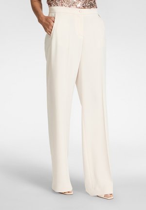 Persona che indossa pantaloni color crema a vita alta e gamba larga con tasche, abbinati a scarpe aperte e top con paillettes.