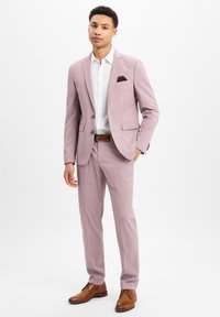 Lichtroze pak met notch-lapels, twee steekzakken, gecombineerd met een wit shirt. Bruine leren schoenen maken de look compleet. Bruine riem inbegrepen.