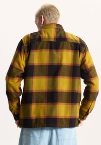 Camicia in flanella a quadri gialli e neri con colletto a bottoni e maniche lunghe, caratterizzata da una vestibilità rilassata e un tessuto texturizzato.