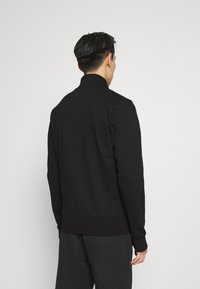 Sudadera negra con cuello alto, diseño ajustado y puños acanalados. Tejido suave y texturizado con detalles mínimos.