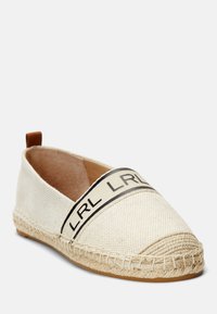 Espadrille de lona con punta redondeada, color crema, banda con logotipo negro en la parte superior y detalles de yute trenzado a lo largo de la suela.