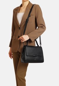 Borsa a mano nera in pelle con un design elegante, forma rettangolare, manico superiore e tracolla staccabile. Texture liscia e accenti hardware minimalisti.