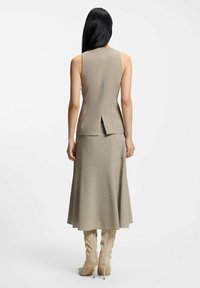 Beżowa dwuczęściowa sukienka z bezrękawnym topem z rozcięciem z tyłu oraz rozkloszowaną spódnicą, uzupełniona dopasowanymi beżowymi botkami za kolano.