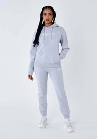 Lichtgrijze hoodie en bijpassende joggers gemaakt van zachte stof, met witte logotekst, een kangoeroezak en ribgebreide boorden bij de enkels en onderkant.