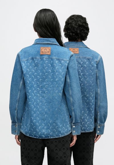 Világoskék színű farmerdzsekik, melyek finom félhold mintával díszítettek a hátoldalon, és világosbarna bőr foltok találhatók a vállakon.