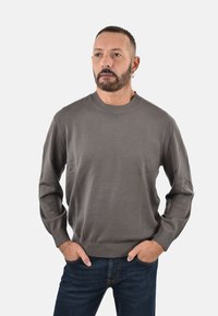 Maglione grigio lavorato a maglia con collo rotondo, polsini e orlo a costine. Abbinato a jeans blu scuro. Il tessuto appare liscio e leggero.