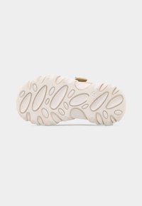 Εξωτερική σόλα μπεζ σανδαλιού με οβάλ και κυκλικά σημεία πρόσφυσης και τον αριθμό μεγέθους 24 ανάγλυφο στη σόλα.