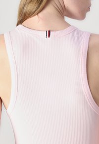 Světle růžový žebrovaný top bez rukávů s kulatým výstřihem, který má pruhovaný detail na zadním výstřihu. Hladká textura.