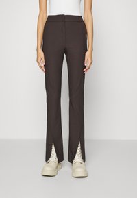 Bruna avsmalnande byxor med sidofickor, gjorda av ett lätt tyg. Har hög midja och bärs med tjocka vita sneakers.