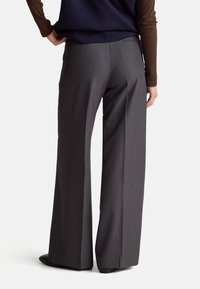 Szerokie spodnie w ciemnoszarym kolorze z gładkiej tkaniny, o dopasowanym kroju i subtelnymi detalami kieszeni z tyłu.
