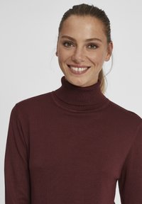 Burgunderfarget genser med høy hals laget av ribbete stoff, med en tettsittende design. Teksturen er glatt, med lange ermer.