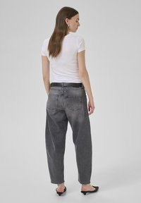 Jeans en denim gris taille haute et coupe ample avec une ceinture noire, dotés de poches arrière et d'une texture délavée, associés à un t-shirt blanc.
