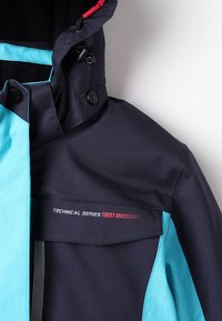 Veste technique bleu foncé et bleu clair avec capuche, poche à rabat et texte "Technical Series 1981" sur la poitrine.