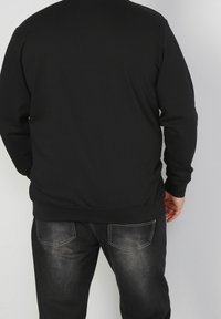 Svart sweatshirt med rund halsringning och långa ärmar, tillverkad av mjukt tyg. Matchad med mörka denimjeans med synliga fickor.