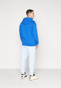 Sweatshirt azul com capuz e um corte relaxado, combinado com calças de treino azuis claras e sapatilhas brancas. Textura suave e design simples.