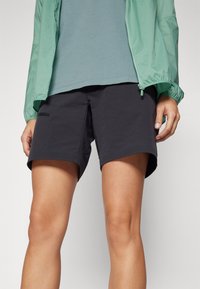 Black shorts with a relaxed fit, made from lightweight fabric, featuring side pockets and a slightly curved hem. Worn with a teal top.