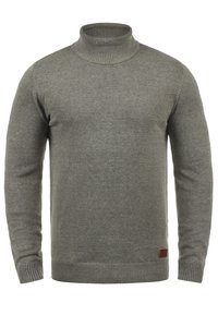 Pull à col roulé gris en tissu tricoté doux. Il présente des bords ribbed aux poignets et à l'ourlet, avec une petite étiquette en cuir marron à la base.