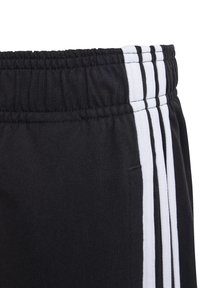 Pantalones deportivos negros con cintura elástica, rayas blancas verticales y textura suave. Incluye un detalle de bolsillo lateral.
