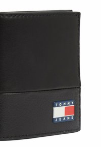 Schwarze Lederbörse mit strukturierter Oberfläche und sichtbaren Nähten. Auffälliges TOMMY JEANS-Logo in Blau, Weiß und Rot.