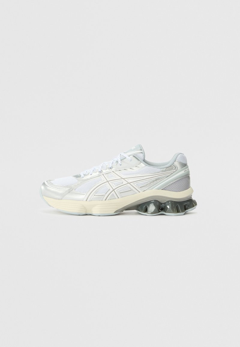 White athletic shoes with a mesh upper, silver accents, and a chunky cushioned sole featuring rounded spikes for support and flexibility.
