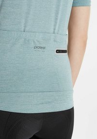 T-shirt de sport bleu clair à manches courtes avec un motif texturé, doté d'une poche zippée et d'une marque discrète au dos.