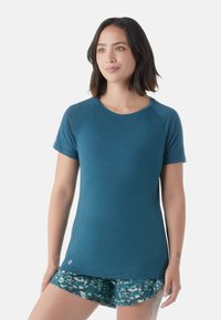Türkises Kurzarm-Sportshirt mit Raglanärmeln, leichtem Material und rundem Ausschnitt. Kombiniert mit gemusterten grünen Shorts.