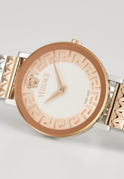 Versace kell, millel on roosakuldne ümar korpus, valge tekstuuriga valge dials, Kreeka võtme muster ja hõbedane käevõru, millel on püramiidi aktsendid. Šveitsi toodang.