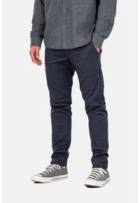 Pantalones de corte slim en azul marino, de mezcla de algodón, con bolsillos y una textura suave, combinados con zapatillas bajas grises.