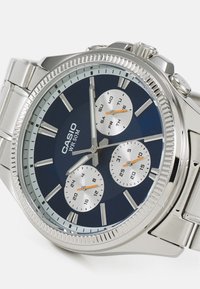 Montre-bracelet Casio WR 50M argentée avec cadran bleu, trois sous-cadrans indiquant le jour, la date et l'heure en format 24 heures, et un bracelet en acier inoxydable.