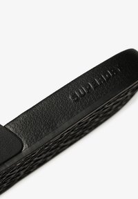 Black rubber slide sandal with a textured surface and the embossed brand name "SUPERDRY" on the strap. Features a breathable design.