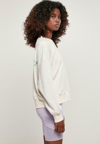 Sudadera gris claro con hombros caídos y dobladillo acanalado, combinada con pantalones cortos ajustados en color lila con bolsillos laterales.