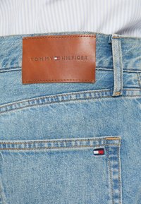 Světle modré denimové džíny s hnědou koženou nášivkou s raženým nápisem "TOMMY HILFIGER" a malou vlajkovou nášivkou na zadní kapse.