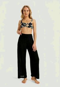 Μαύρο crop top με λουλουδάτο σχέδιο και λεπτές ράντες, συνδυασμένο με ελαφριά, φαρδιά μαύρα παντελόνια με ριμπ ζώνη.