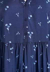 Mornarsko modra obleka z svetlo modrim cvetličnim vzorcem, nabrana pas in črne gumbe spredaj.