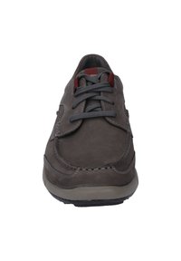 Scarpa in suede marrone con lacci grigi, caratterizzata da una punta arrotondata, cuciture decorative e una suola in gomma. Accento rosso vicino alla linguetta.