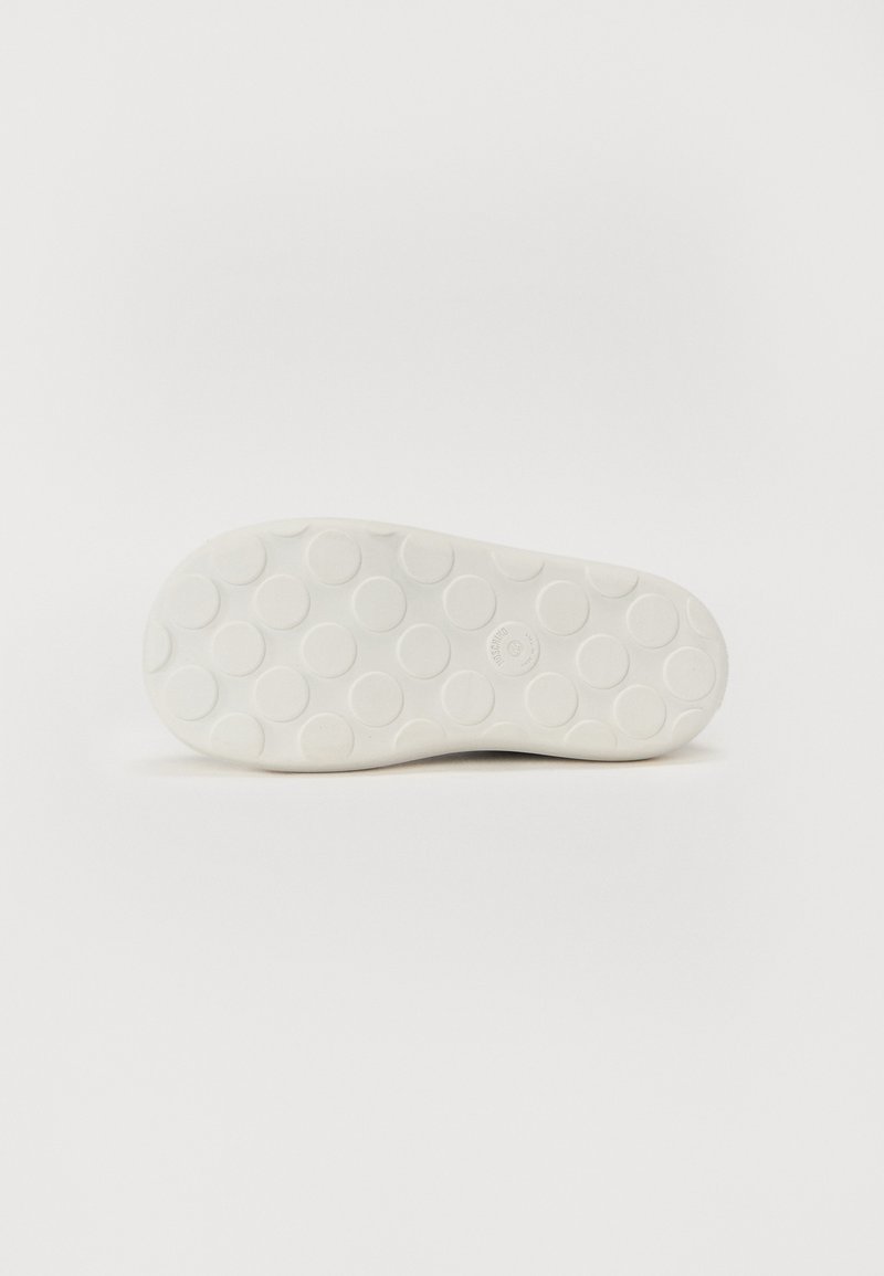 Witte rubberen zool van een schoen met een cirkelpatroon en verhogingen in de vorm van stippen, ontworpen voor grip en tractie. Gladde textuur met een afgeronde vorm.