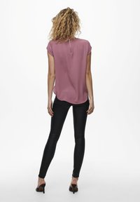 Blusa rosa a maniche corte con scollo rotondo e zip sul retro. Abbinata a pantaloni neri aderenti e tacchi alti.