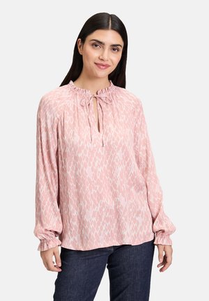 Lichtroze blouse met een gestructureerd patroon, gegooide halslijn en strikdetail. Beschikt over lange mouwen met elastische manchetten.