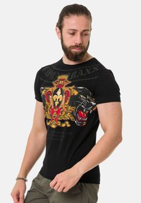 Schwarzes T-Shirt mit kurzen Ärmeln und buntem Grafikdesign, das eine Krone, Lilie und einen Panther zeigt. Hergestellt aus Baumwolle mit glatter Textur.