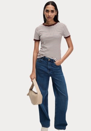 T-shirt rayé avec des accents bordeaux, associé à un jean large bleu. Sac à main beige de forme arrondie. Baskets blanches.