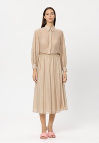 Beige, long-sleeve, button-up dress with a gathered waist, pleated skirt, textured fabric. Pink open-toe slides complete the look.